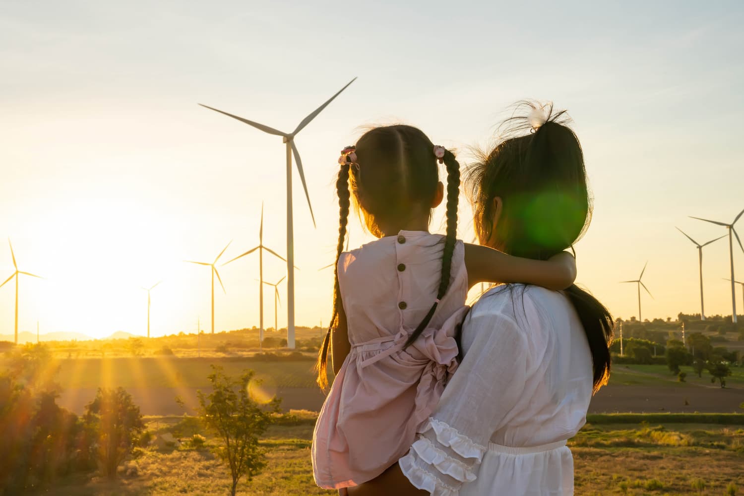 Mujer y su hija frente a aerogeneradores, simbolizando el avance de la tecnología sostenible en la energía renovable.